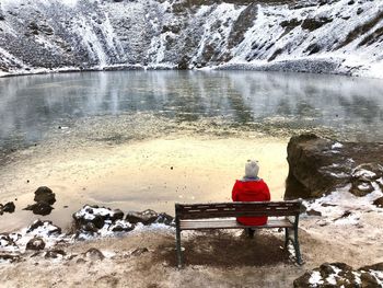 Rear view of man sitting on bench by lake