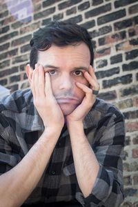 Portrait of worried man with hands on chin against brick wall