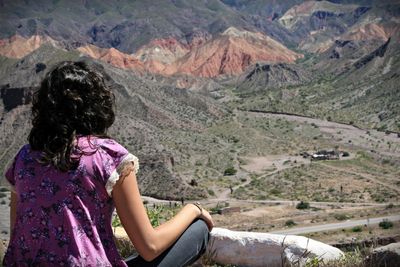 Girl sitting on landscape against mountains