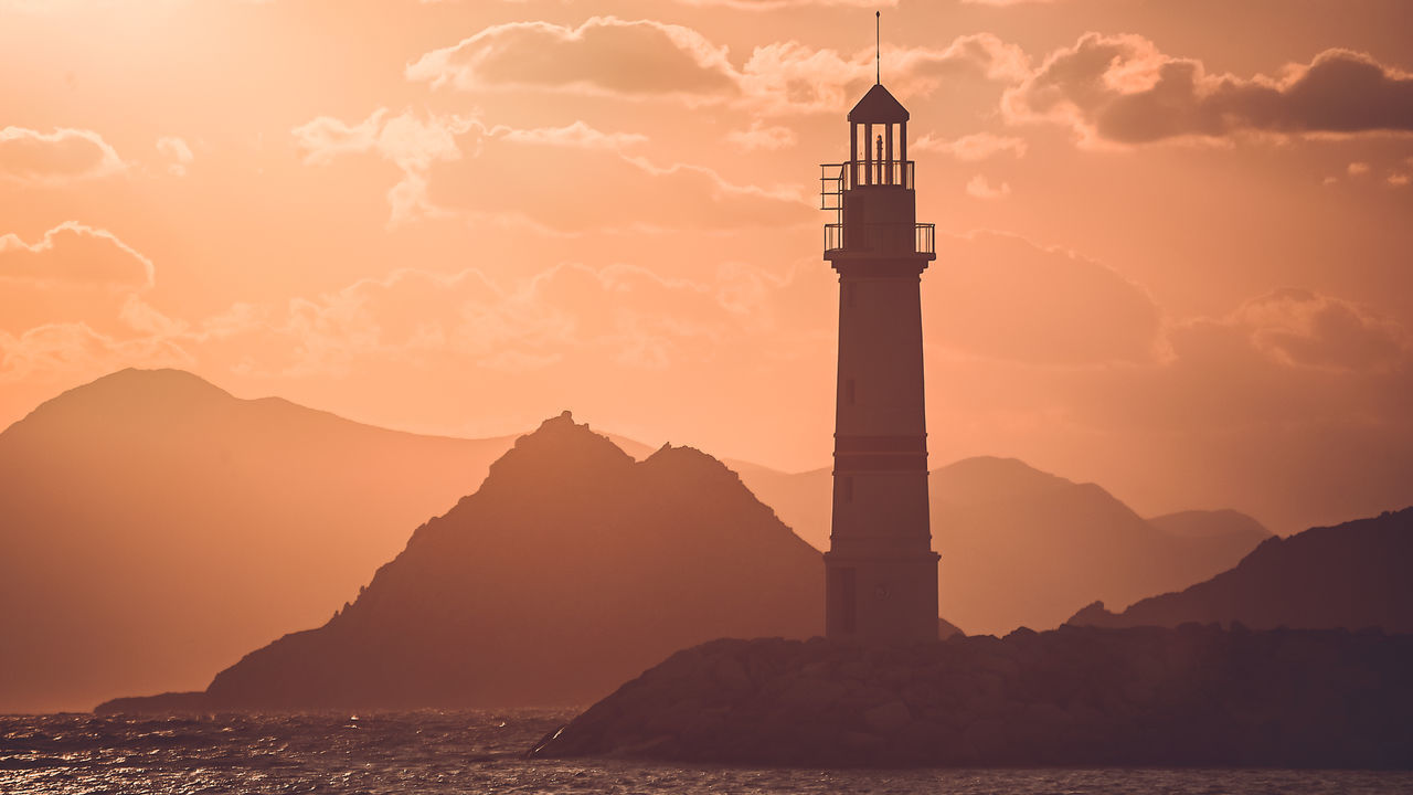 LIGHTHOUSE BY SILHOUETTE MOUNTAIN AGAINST SKY DURING SUNSET
