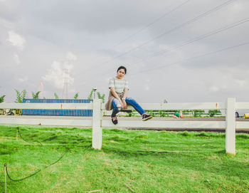 Young woman sitting on grass against sky