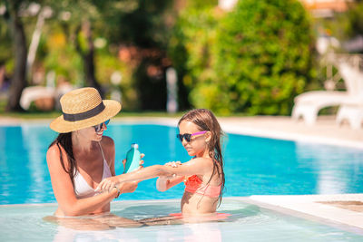 Mother applying suntan lotion to daughter at swimming pool