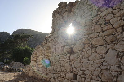 Low angle view of sun shining through rocks against clear sky