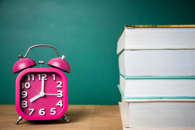 Close-up of alarm clock and books on table against green chalkboard