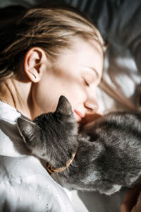 Candid portrait of young woman is resting with kitten pet on the bed at home one sunny day.