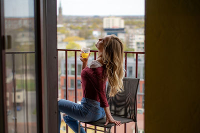 Rear view of woman drinking glass while sitting in window