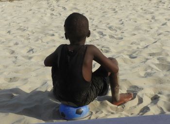 Rear view of boy sitting on sand at beach