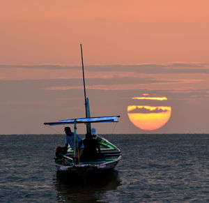 Men sailing boat in sea against orange sky during sunset
