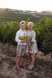 Mother and her teenage son are standing in a vineyard wicker basket and green grapes in nature