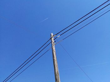 Low angle view of electricity pylon against blue sky