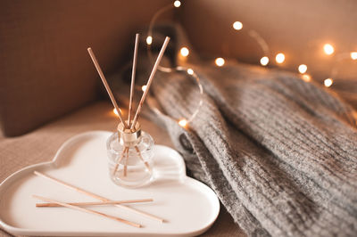 Liquid home perfume in glass bottle with wooden bamboo stick and burn candle on white ceramic tray