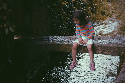 Full length of girl sitting on stone over stream