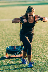 Full length of woman pulling weight on grassy field