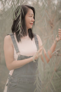 Young woman with arms raised standing against plants