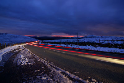 Light trails on road against sky at night