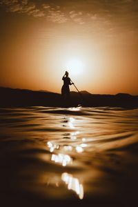 Silhouette person in sea against sky during sunset