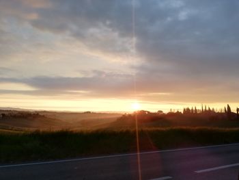 Road amidst field against sky during sunset