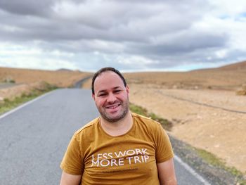 Portrait of smiling man standing on road against sky