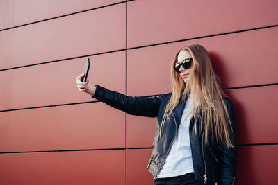 Woman taking selfie while standing against red wall