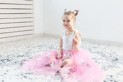 Portrait of cute girl sitting on pink indoors