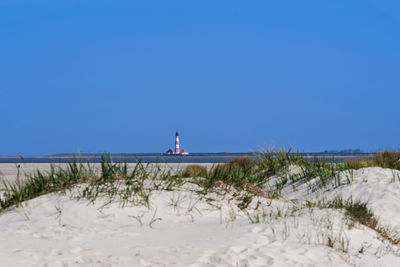 Lighthouse on field against clear blue sky during winter