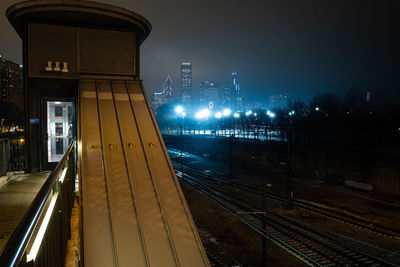 Illuminated railroad station in city against sky at night