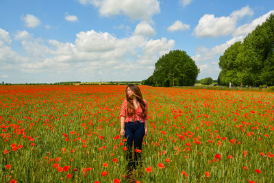 Rear view of woman by poppy field against cloudy sky