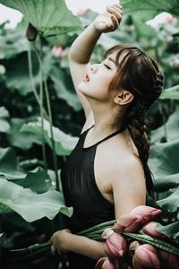 Young woman looking down while standing against plants