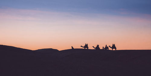 Silhouette people on desert against sky during sunset