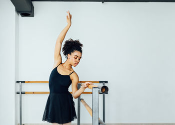 Young woman practicing ballet by railing in studio