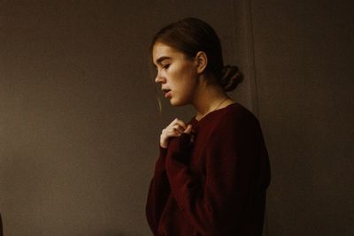 Side view of young woman looking away against wall