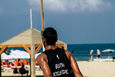 Rear view of men at beach against sky