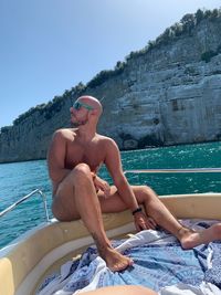 Full length of shirtless man sitting in sea against sky