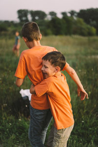 Funny boys brothers in a orange t-shirt playing outdoors on the field at sunset