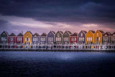 Houses by sea against sky during sunset