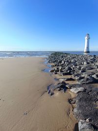 Lighthouse on beach against blue sky