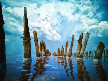 Panoramic view of wooden posts on water against sky