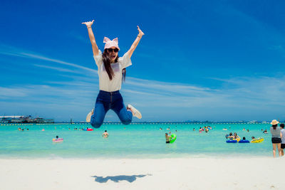 Full length of young woman enjoying at beach against blue sky