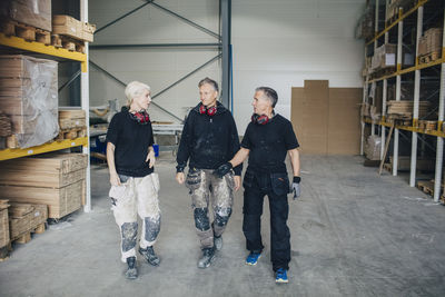 Full length of confident workers walking amidst racks in lumber industry