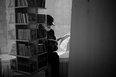 Side view of man reading book against wall at home