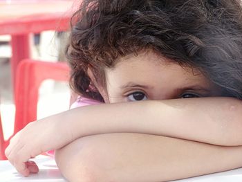 Portrait of girl covering face with arms while leaning on table