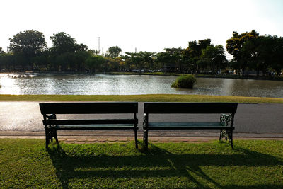 Bench by lake in park against clear sky