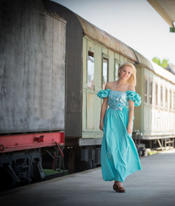 Portrait of young woman wearing blue dress while walking on railroad station platform