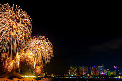 Firework display over illuminated buildings against sky at night