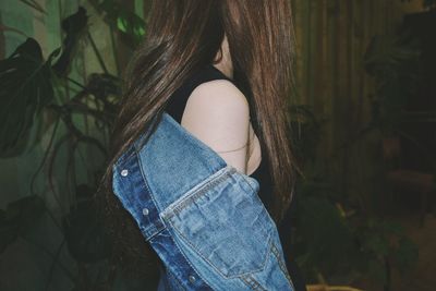 Side view of woman wearing denim jacket while standing against plants