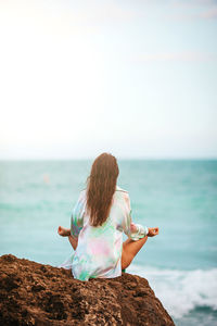 Rear view of woman sitting at beach against clear sky