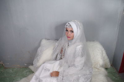 Portrait of bride wearing traditional clothing sitting against wall