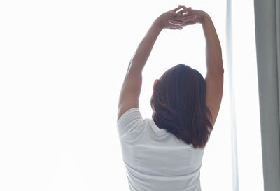 Rear view of woman with arms raised standing against white background