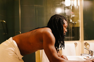 Thoughtful shirtless man bending at sink in bathroom