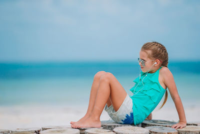 Boy sitting at beach against sky